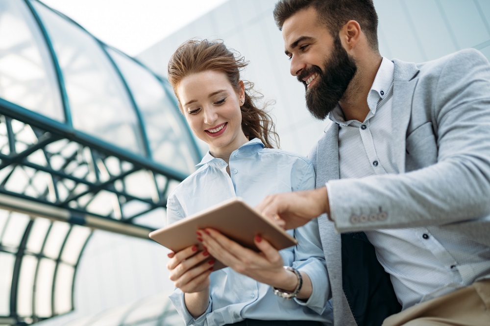 Junior Account Manager Mann und Frau schauen draußen auf ein Tablet